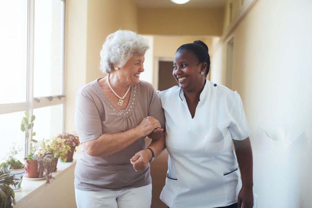 smiling home caregiver and senior woman walking together through a corridor